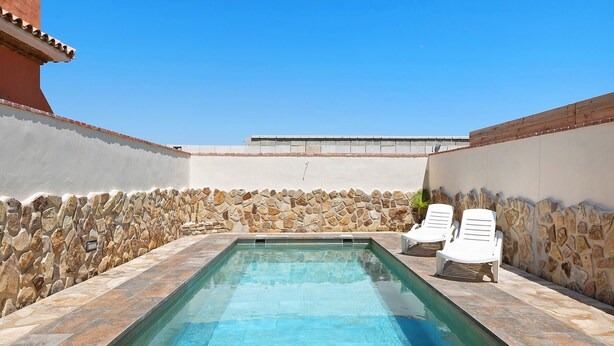 A rectangular swimming pool with stone walls and a tiled deck, surrounded by white lounge chairs. - Holiday Home "Casa Juana Madera" with Shared Pool and Air Conditioning (Zahora)