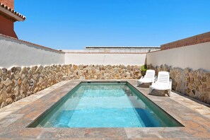 A rectangular swimming pool with stone walls and a tiled deck, surrounded by white lounge chairs. - Holiday Home "Casa Juana Madera" with Shared Pool and Air Conditioning (Zahora)