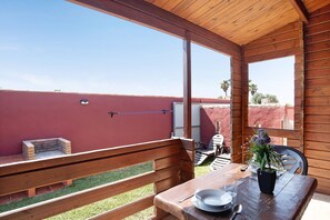 Une terrasse en bois avec un barbecue, une table agrémentée d’une plante en pot et une chaise.