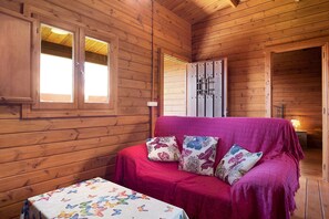 L’intérieur d’un chalet en bois, avec un canapé rouge, une table recouverte d’une nappe à motifs papillons et une armoire dotée de poignées en métal.