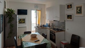 A compact kitchen with a dining area, a refrigerator, a stove, and a clock on the wall. - Holiday Apartment "Violet House" with Private Terrace, Air Conditioning and Wi-Fi (Catania)