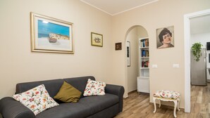 A living room with a sofa, a small bench, a bookshelf, and a framed picture on the wall. - Holiday Apartment "Violet House" with Private Terrace, Air Conditioning and Wi-Fi (Catania)