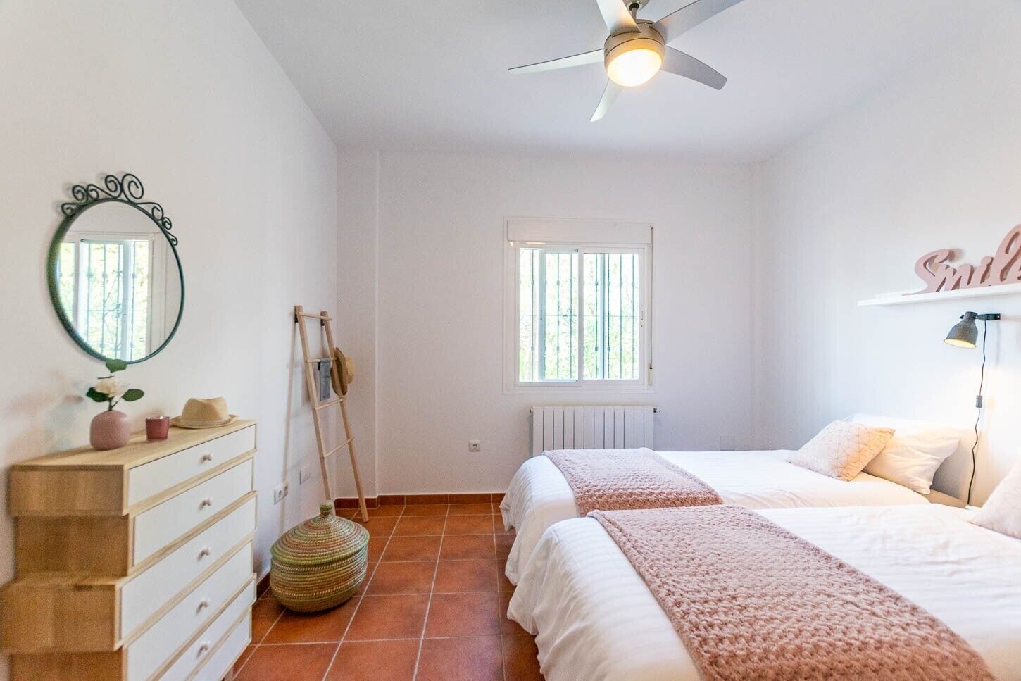 Un dormitorio con dos camas, ventilador de techo, ventana, cómoda y espejo.