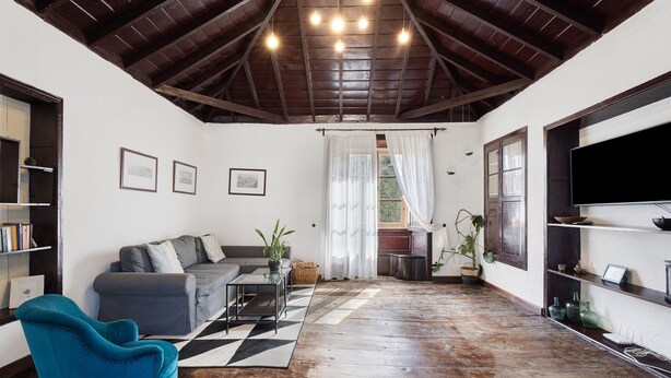 A living room with a sofa, a blue chair, a coffee table, a TV, and a wooden ceiling. - Vacation Home "Casa Rural El Palmar" with Mountain View, Private Terrace & Wi-Fi (Vallehermoso)