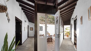 A corridor with a door leading to an outdoor patio area, a chair, and a table with potted plants. - Vacation Home "Casa Rural El Palmar" with Mountain View, Private Terrace & Wi-Fi (Vallehermoso)