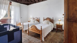 A room with two wooden beds, a small table, a chair, and a window with curtains. - Vacation Home "Casa Rural El Palmar" with Mountain View, Private Terrace & Wi-Fi (Vallehermoso)