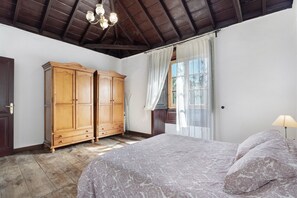 A bedroom with a large bed, wooden wardrobe, and a chandelier. - Vacation Home "Casa Rural El Palmar" with Mountain View, Private Terrace & Wi-Fi (Vallehermoso)