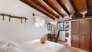 A bedroom with a bed, a wooden headboard, a stone wall, and a wardrobe.