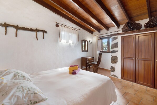 A bedroom with a bed, a wooden headboard, a stone wall, and a wardrobe.