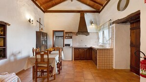 A rustic kitchen with wooden beams, a tiled backsplash, and a dining area with a table and chairs.