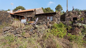 A stone house with a sloped roof, a small porch with a chair, and a stone wall.