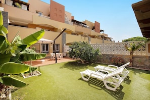 Cortile di un hotel con erba sintetica, poltroncine bianche e un tavolino.