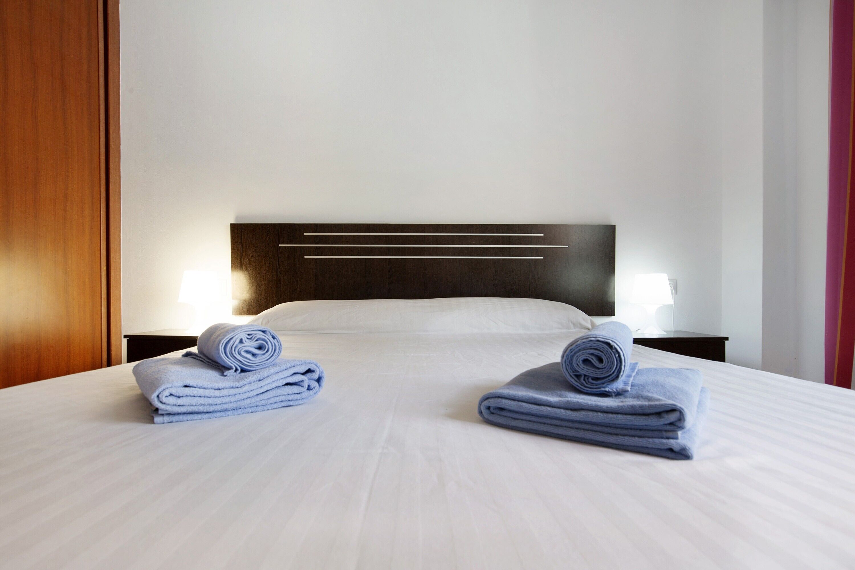 Een hotelkamer met een net opgemaakt bed, een houten hoofdeinde en twee nachtkastjes met lampen.
