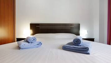 Een hotelkamer met een net opgemaakt bed, een houten hoofdeinde en twee nachtkastjes met lampen.
