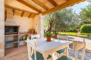 An outdoor patio with a brick fireplace, white table, and chairs, surrounded by greenery. - Country House 'Es Revolt De Sa Barrala' with Private Pool, Wi-Fi and Air Conditioning (Campos)