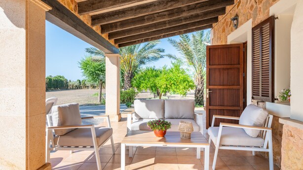 Eine Terrasse im Freien mit einer Couch, Sesseln, einem Tisch und einem Blumentopf.