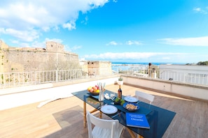 A dining table set outdoors with a view of a historic fort and the sea. - Casa Sveva A Otranto Sea View Holiday Home with Private Terrace and Air Conditioning (Otranto)