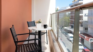 Ein Balkon mit Tisch, zwei Stühlen, einer Blumenvase und einer schwarzen Tasse.