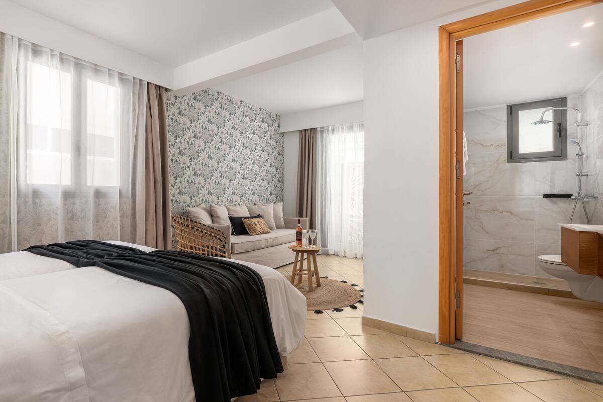 Ein modernes Schlafzimmer mit einem großen Bett, einer Couch, einem kleinen Tisch mit Gläsern und einem Badezimmer mit Dusche und Toilette.
