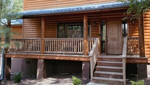 Een vakantiehuisje van hout met een veranda, schoorsteen en een groot raam.