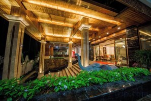 Un espace extérieur abrité comprenant un banc en pierre, un escalier en bois et une porte vitrée donnant sur l’intérieur.