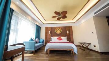 A hotel room with a bed, a desk, a chair, a ceiling fan, and a window with curtains.
