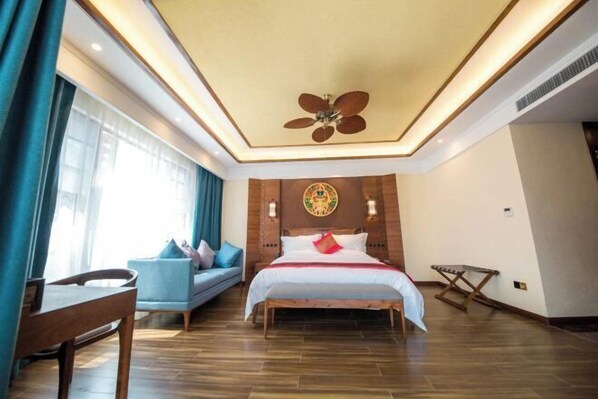 Une chambre d’hôtel équipée d’un lit, d’un bureau, d’une chaise, d’un ventilateur de plafond et d’une fenêtre avec des rideaux.