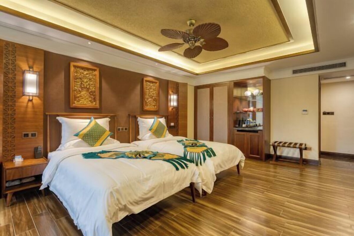 Une chambre d’hôtel avec un grand lit, deux tables de chevet, un ventilateur de plafond et un plancher en bois.