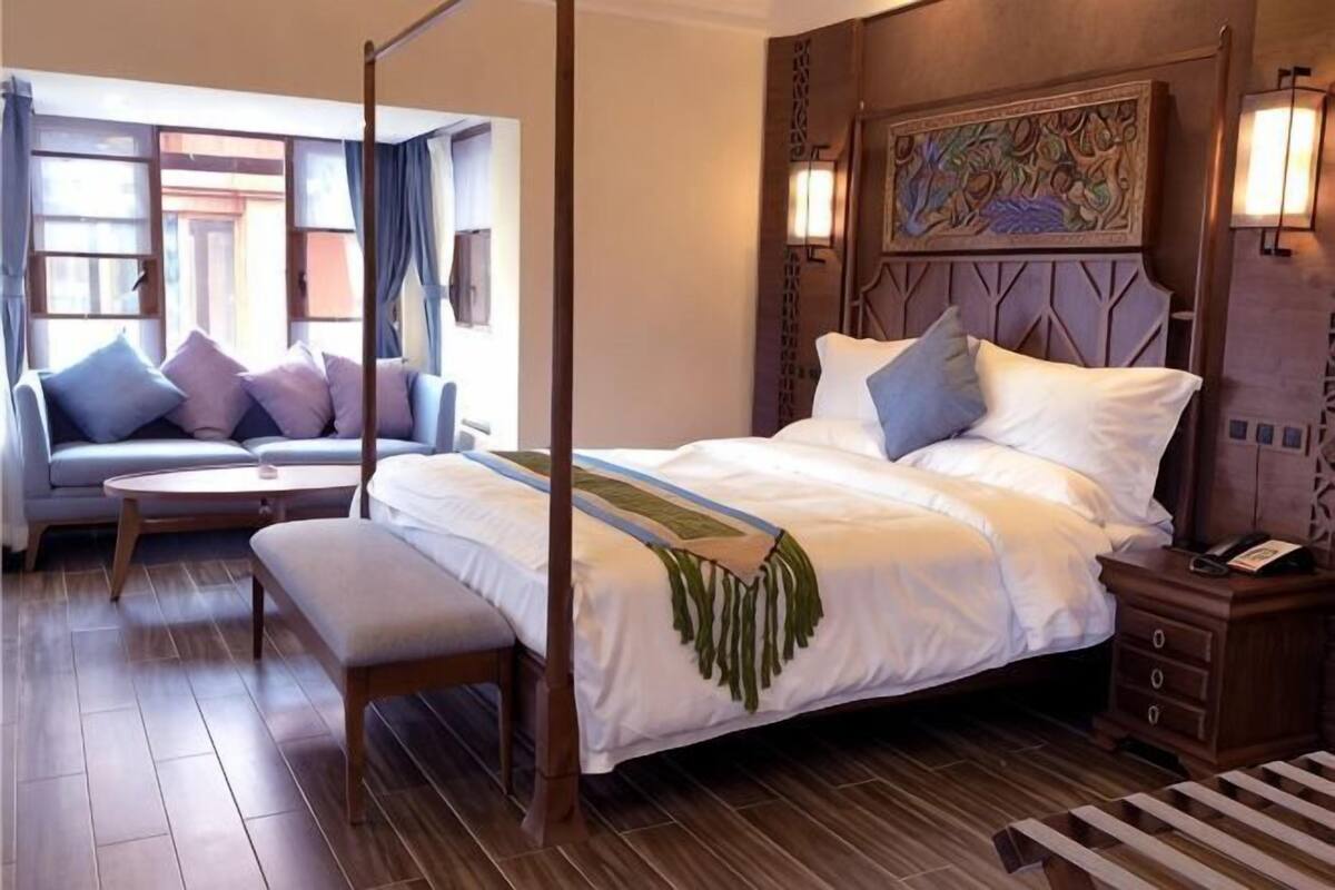 Een kamer met een hemelbed, een bank, een kleine tafel, houten vloeren en een decoratief hoofdeinde.