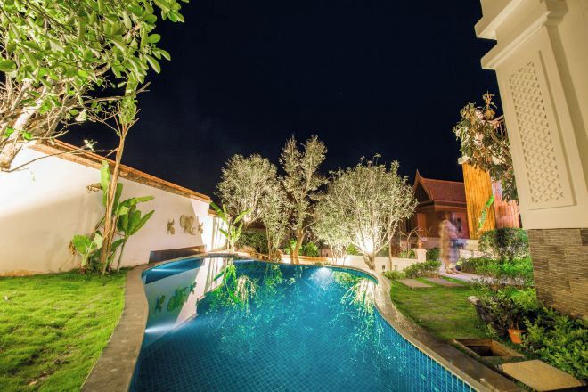 Piscina rodeada por un jardín bien cuidado, con una casa al fondo.