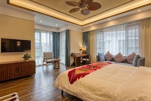 Camera d'albergo con un letto grande, una scrivania, una sedia, una TV e una ventola a soffitto.