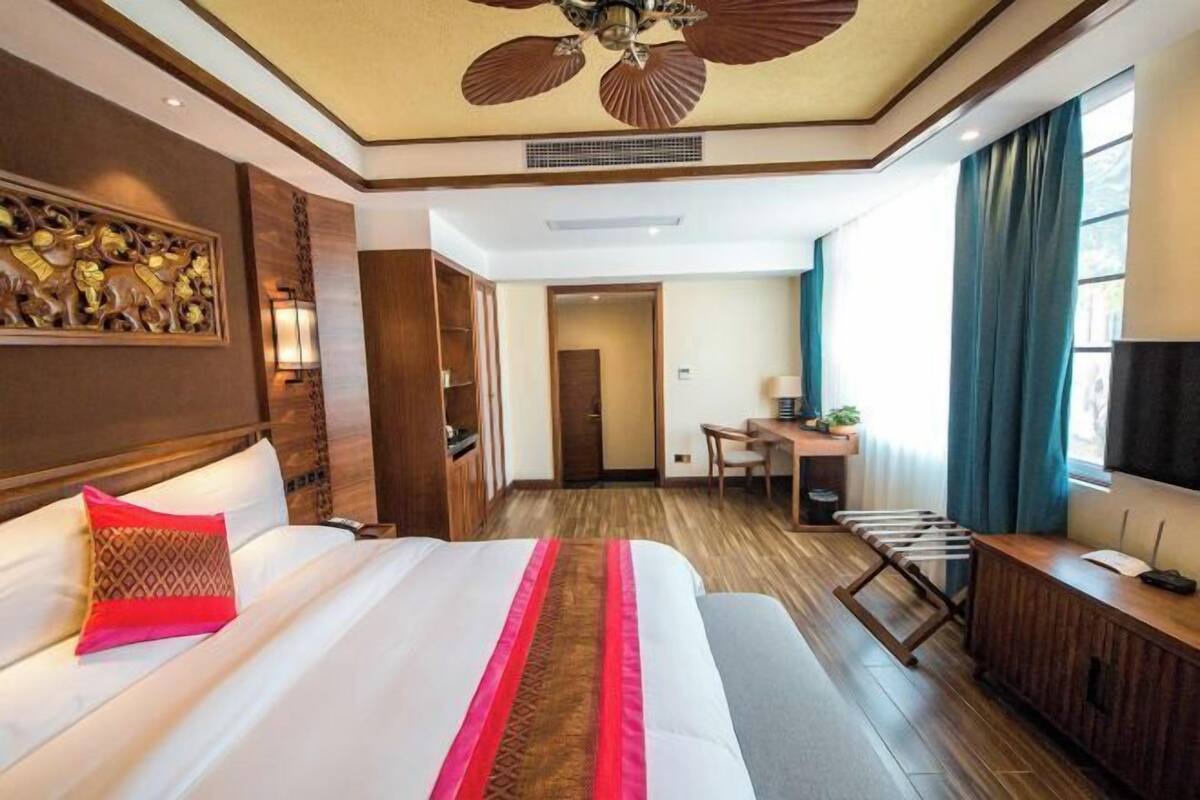 Een hotelkamer met een groot bed, een bureau, een stoel, een televisie en een plafondventilator.