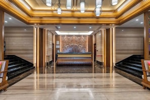 Vestíbulo de hotel con mostrador de recepción, suelo de mármol y una escalera.