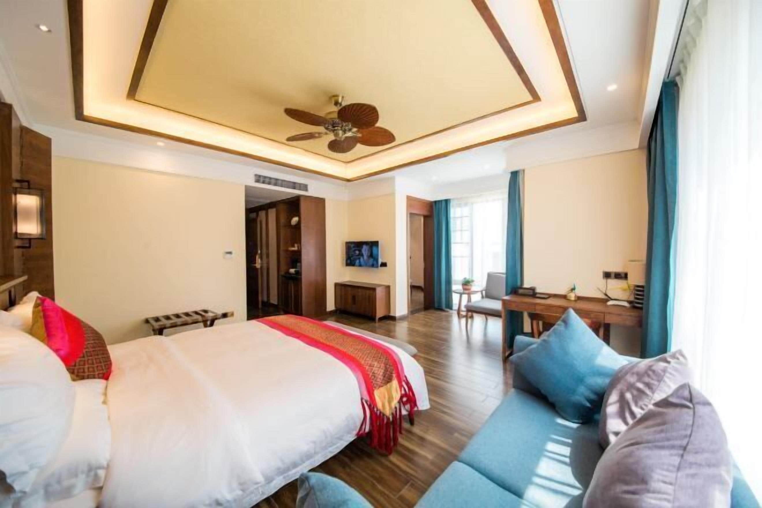 Ein Hotelzimmer mit einem großen Bett, einer Couch, einem Schreibtisch und einem Deckenventilator.