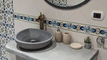 Une salle de bain avec un lavabo en pierre, un miroir rond et un mur recouvert de carreaux décoratifs.