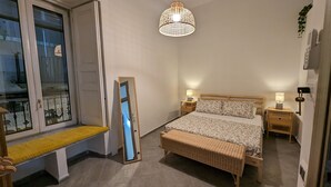 Un dormitorio con cama, mesitas de noche, un banco, una lámpara colgante y ventana con vistas.