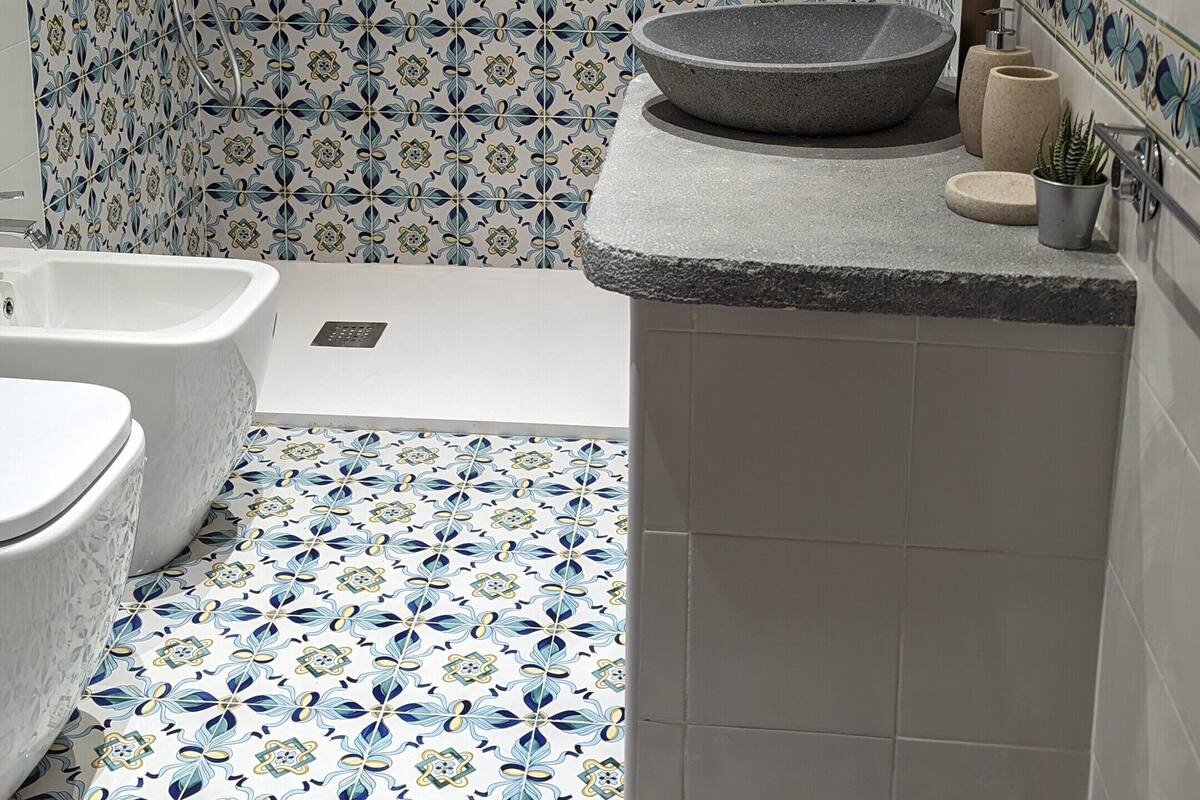 Ein Badezimmer mit einem Fliesenrückwand mit Muster, einem runden Waschbecken mit Natursteinbecken, zwei freistehenden Badewannen auf Ziegenfüßen und einer Handbrause.