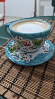 Una taza y platillo de cerámica con diseños florales sobre un tapete tejido.