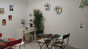 Comedor con mesa roja, sillas negras, planta en maceta y adornos de pared que incluyen platos y pósters.