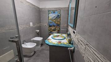 A bathroom with a toilet, bidet, and a sink with a decorative tile backsplash.
