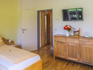 A hotel room with a bed, wooden wardrobe, a television mounted on the wall, and a door leading to another room. - Appartement Gerlitzen - Pension Strauß (Rappitsch)