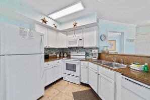Fully equipped kitchen with refrigerator, microwave, oven, and coffee maker, featuring a sink with a stainless steel faucet and a mosaic backsplash.