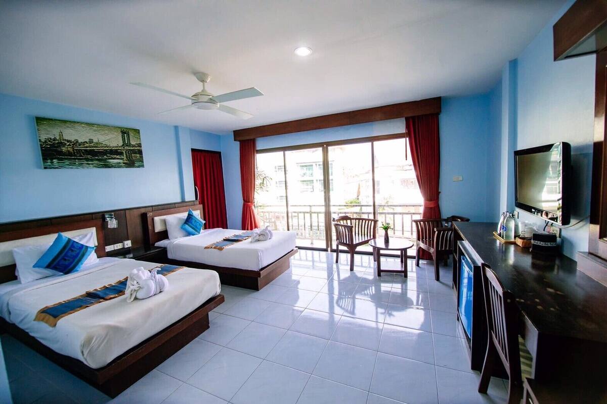 A hotel room with two beds, a balcony, a TV, and a dining area.