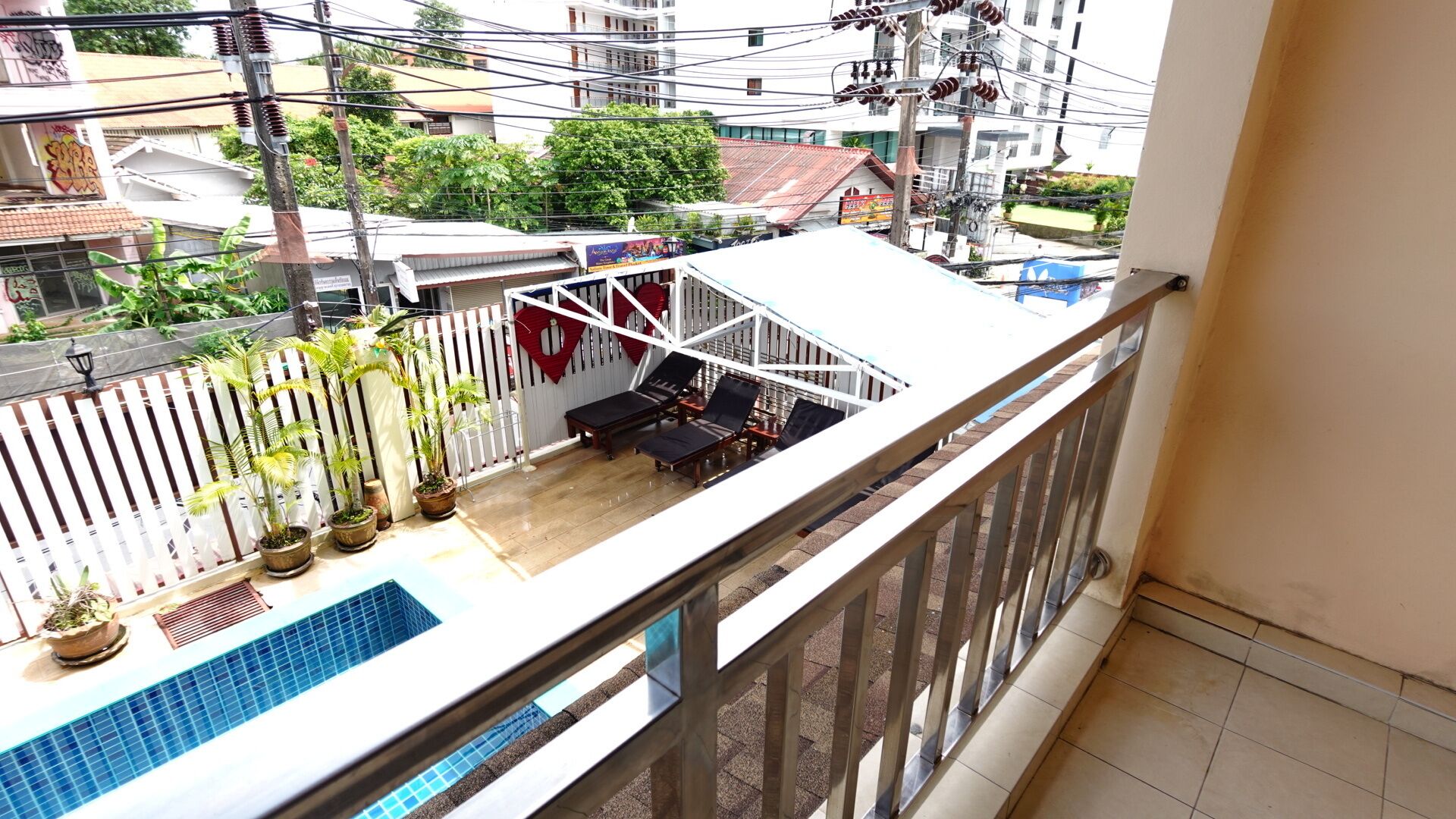 Un balcon avec une piscine, des plantes en pot et un espace détente agrémenté d’une clôture blanche et de décorations rouges.
