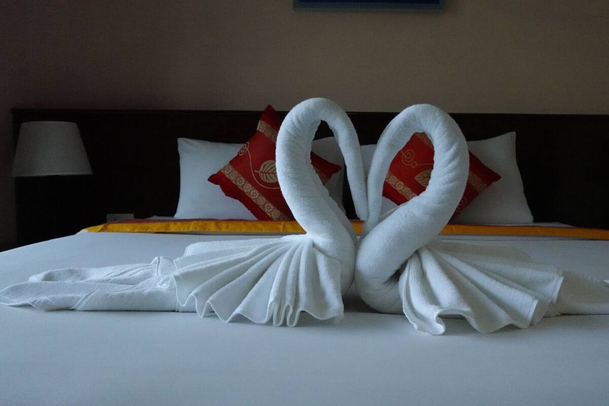 A bed with white linens and two towels arranged in a heart shape.