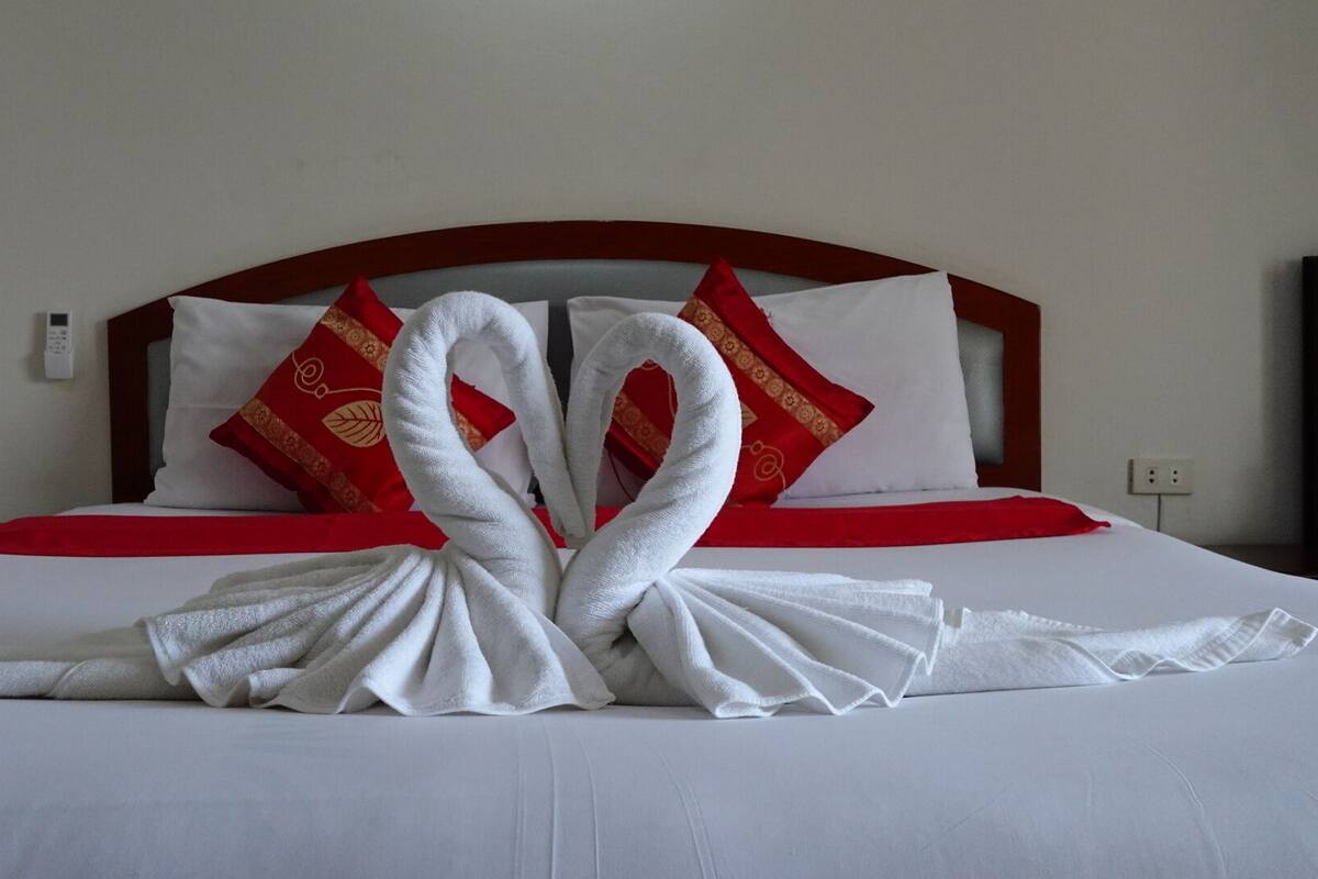 A hotel room with a neatly made bed, red and white pillows, and a red bedspread.