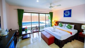 A hotel room with a bed, a desk, a chair, a small table with a vase, and a balcony with a view of a pool and a wooden fence. - Wanna Marine (Patong)