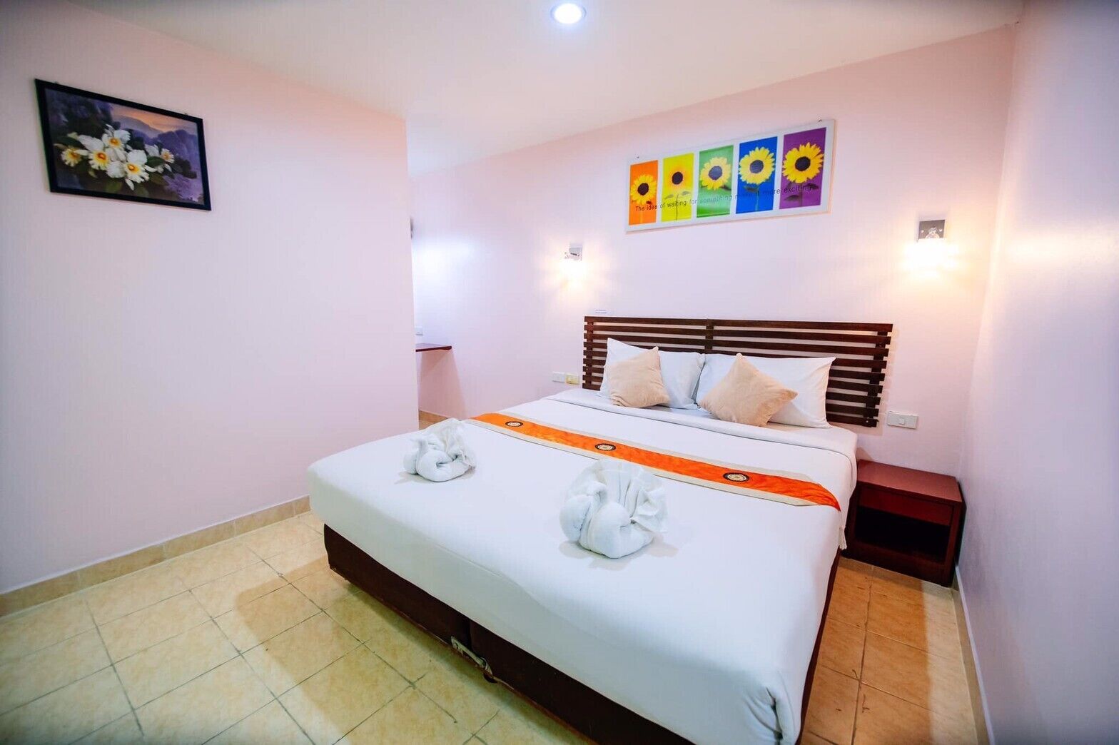 Ein Hotelzimmer mit Bett, Kissen, einem Nachttisch, einem Wandbild und einem gefliesten Boden.