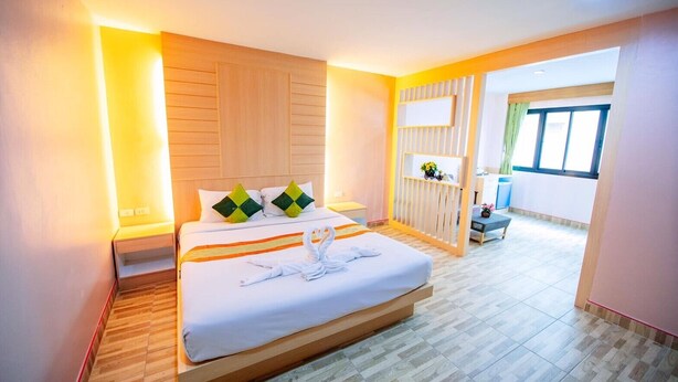 A hotel room with a large bed, wooden headboard, and a view of a balcony. - Wanna Marine (Patong)