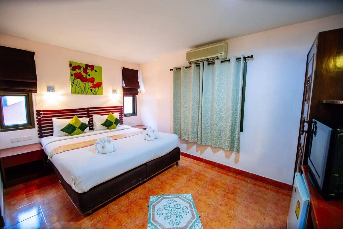 A hotel room with a bed, a window, a wall-mounted air conditioner, and a television.